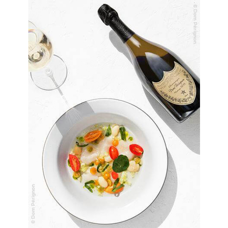une bouteille de dom perignon vintage 2013 sur une table à côté d'un plat et un verre de champagne