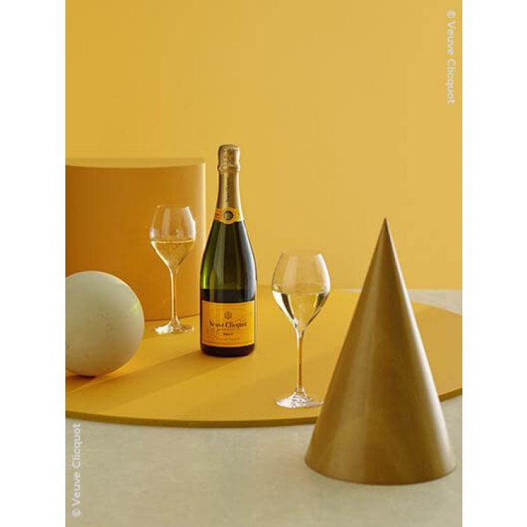 bouteille de veuve clicquot brut carte jaune sur une table orangée avec des flutes et formes différentes